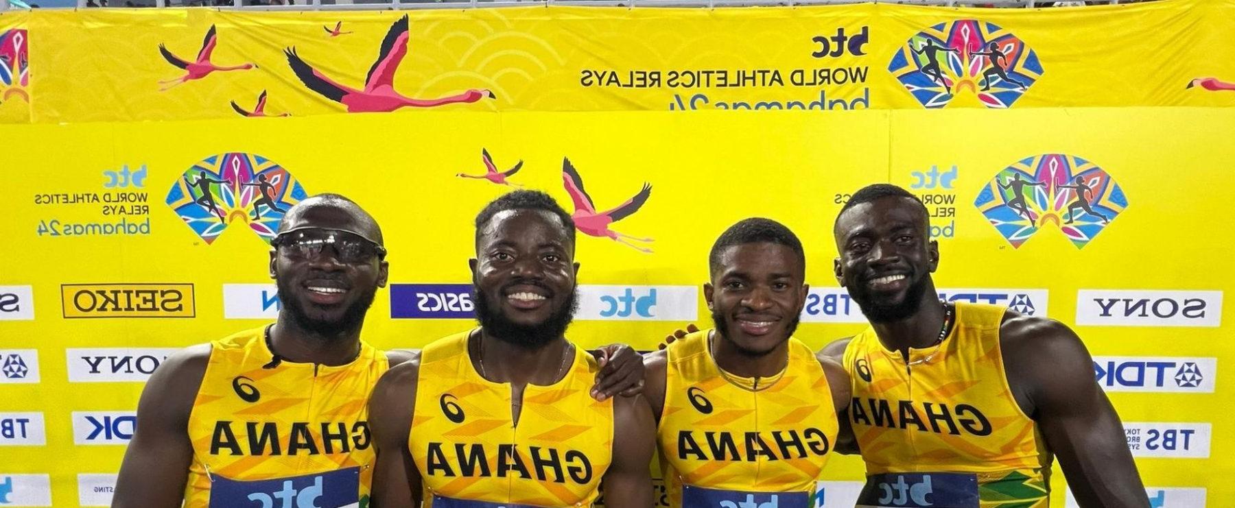 Four athletes pose before a yellow background, wearing their yellow Ghana jerseys and smiling with their arms around each other.